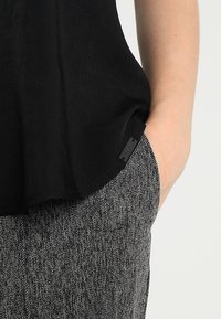 Svart, löst sittande topp med mjuk textur, med en sidetikett, kombinerad med grå tygbyxor i houndstooth-mönster.