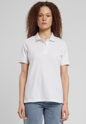 Weißes Baumwoll-Poloshirt mit Kragen, das eine Knopfleiste und kurze Ärmel hat. Kombiniert mit hellblauen Jeans aus Denim.