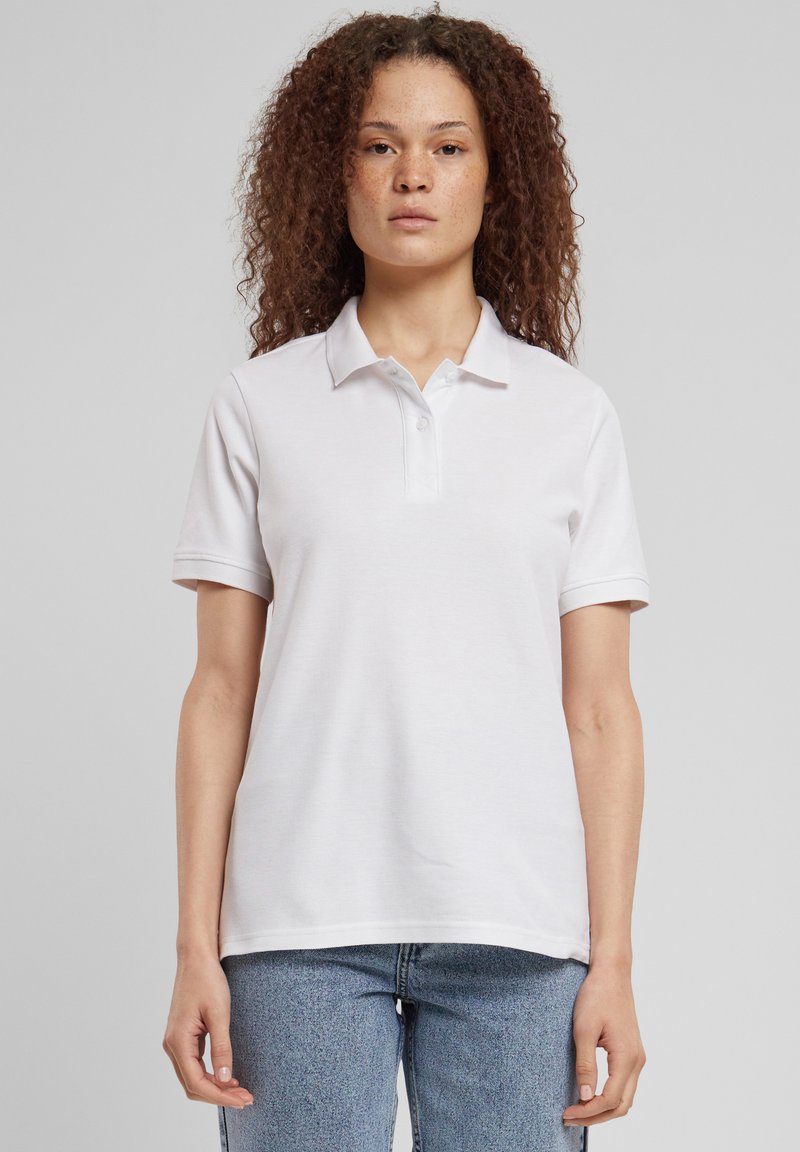 Bijela polo majica od pamuka s ovratnikom, s gumbima na prednjoj strani i kratkim rukavima. Nošena s svijetloplavim trapericama.