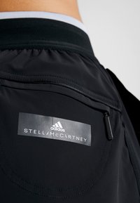 Svarta träningsshorts med en mjuk textur, elastisk midja och en blixtlåsficka. Märkningen inkluderar "adidas" och "STELLA McCARTNEY."