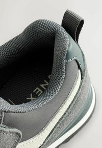 Gray sneaker with textured mesh upper, smooth leather accents, and a pull tab. Features a white midsole and a patterned inner lining.