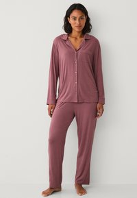 Lichtgewicht bordeauxrood loungewear set met een lang mouwen knoopsluiting bovenstuk met pocket en bijpassende broeken, gemaakt van zachte stof met een gladde textuur.