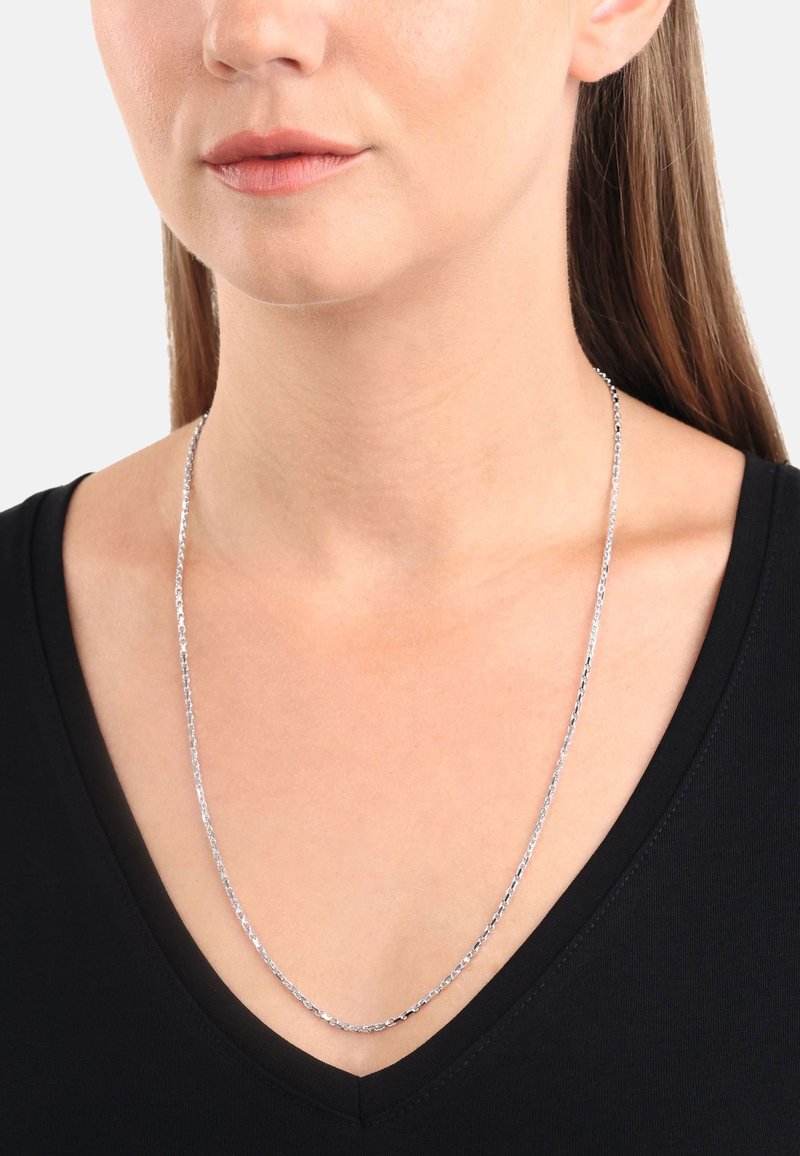 Silverfärgad kedjehalsband med en subtil länkdesign, som bärs runt halsen, som kompletterar en svart V-ringad topp. Slät yta och reflekterande finish.