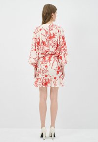Bloemrijke jurk met rode en witte kleuren, met brede mouwen en een uitlopend zoom, gecombineerd met crèmekleurige blokhakken.