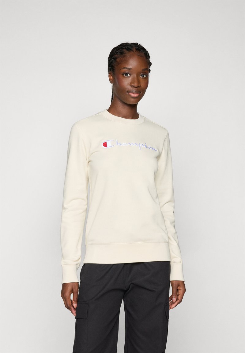 Cremfarbener Sweatshirt aus weichem Material mit Rundhalsausschnitt. Mit gesticktem "Champion"-Logo in Rot, Blau und Weiß. Enganliegende Bündchen und Saum.