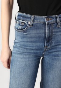 Light blue denim jeans with a high waist, five-pocket design, and a button closure. Visible stitching and slight fading on the fabric.