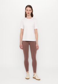 Hvit bomull t-skjorte, rund hals, korte ermer, kombinert med brune tettsittende leggings og lyse beige snøresko.