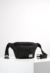 Černá nylonová ledvinka s nastavitelným popruhem, přední zipovou kapsou a logem. Disponuje hladkým povrchem a minimalistickým designem.