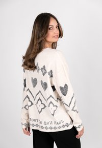 Cremefarbener Pullover mit schwarzen Mustern, einschließlich Herzen und geometrischen Formen, mit weitem Schnitt und weichem, strukturiertem Stoff.
