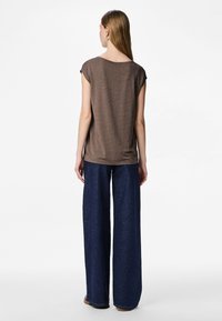 Ruskea lyhythihainen toppi, jossa rento istuvuus, hienovarainen tekstuuri ja pyöreä pääntie, yhdistetty leveälahkeisiin tummansinisiin denimhousuihin.