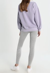 Lila oversized sweatshirt, grå leggings med vitt Nike-logo, kombinerat med vita sneakers. Fokus på avslappnad, bekväm sportklädsel.
