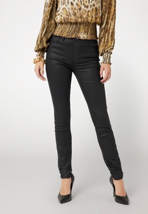 Pantalones ajustados de imitación cuero negros con una textura suave, que presentan una cintura de altura media y un ajuste ceñido, combinados con tacones de aguja negros.