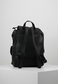 Czarny skórzany plecak o teksturowanym wykończeniu, z regulowanymi ramiączkami i sznurkiem u góry. Posiada podwójne kieszenie boczne oraz minimalistyczny design.