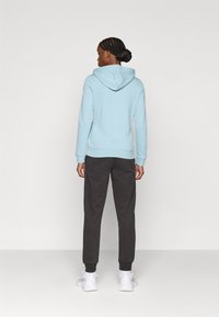 Ανοιχτό μπλε φούτερ με κουκούλα και κορδόνι, μανσέτες ριμπ, συνδυασμένο με σκούρα γκρι φόρμα. Φορεμένο με λευκά αθλητικά παπούτσια.