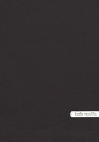 Zwarte katoenen T-shirt met een zachte textuur en een zilveren logo-tag met de tekst "bazix republiq" dicht bij de zoom.