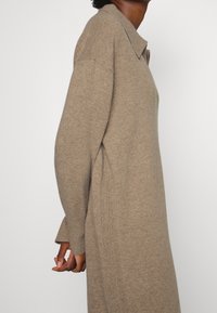 Beige stickad klänning med krage, långa ärmar och ribbade detaljer på sidorna. Mjuk textur och avslappnad passform.