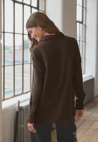 Brown, long-sleeve button-up shirt with a collar, smooth texture, and slight sheen. Features a back yoke and fitted cuffs.