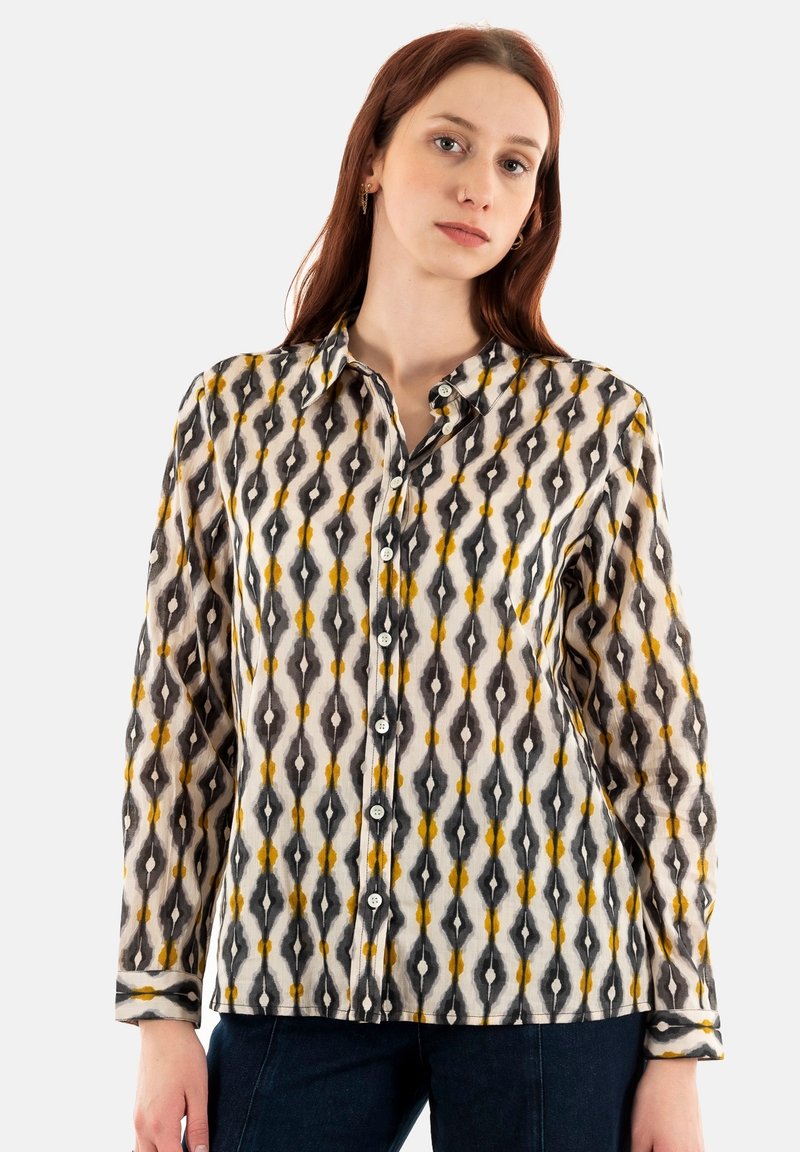 Camisa de manga larga con botones en tejido ligero que presenta un patrón geométrico en tonos negros, blancos y amarillos, con un cuello tipo camisa.
