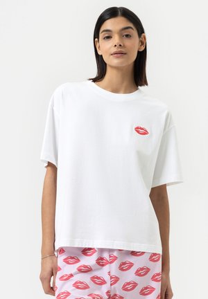 T-shirt en coton blanc avec une coupe oversize, encolure ronde et un design de lèvres rouges sur la poitrine. Associé à un bas à motifs comportant des lèvres roses.