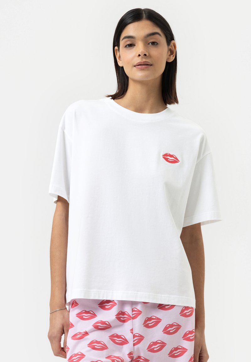 Witte katoenen t-shirt met een oversized pasvorm, ronde hals en een ontwerp van rode lippen op de borst. Gecombineerd met een patroon onderstuk met roze lippen.