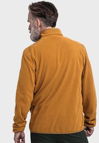 Fleece-Pullover in senfgelb mit hohem Kragen, langen Ärmeln und strukturierter Oberfläche. Verfügt über dezente grüne Nähte am Kragen.