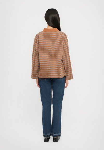 Striped, long-sleeve top in warm tones with a collar; paired with flared dark blue jeans. Smooth texture, casual design, and relaxed fit.