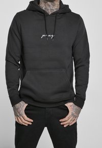 Schwarzer Kapuzenpullover aus glattem Stoff, mit einer vorderen Kängurutasche und dem Schriftzug "pray." in weißer Schrift. Eng anliegende Bündchen und Saum.