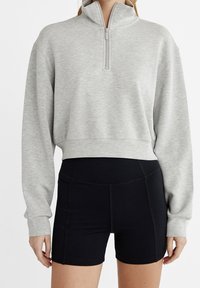 Grå, kort sweatshirt med hög krage och framzippert, kombinerad med svarta högmidjade shorts med texturerad tyg och sömnadsdetaljer.