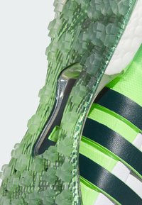 Zapatilla deportiva verde con un upper texturizado que presenta acentos geométricos, rayas negras y una suela multi-agarre para una mejor tracción.