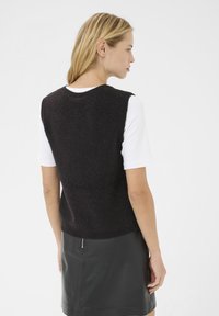 Top senza maniche di maglia nera con finitura testurizzata, indossato sopra una camicia bianca a maniche corte, abbinato a una gonna di pelle nera.