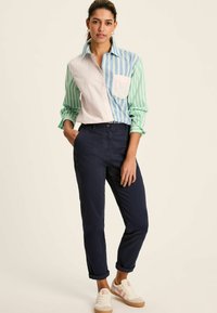 Lekka, pasiaste koszula z guzikami w kolorze zielonym i niebieskim, zestawiona z granatowymi chinosami i beżowymi butami, z podwiniętymi rękawami i bocznymi kieszeniami.