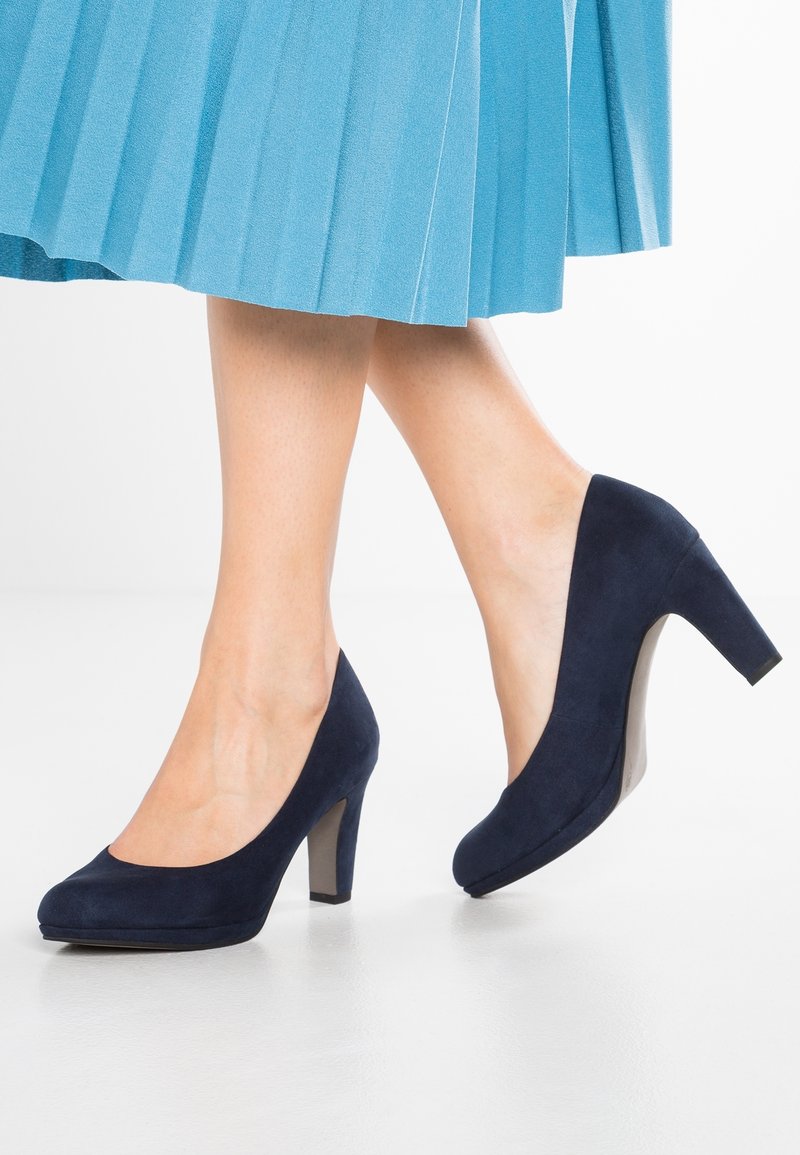 Des escarpins en suède bleu marine avec un bout rond et un talon bloc robuste. Ils présentent une texture lisse et une plateforme légèrement surélevée.