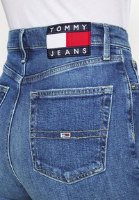 Blå denimjeans med hög midja, med en röd, vit och blå märkeslapp på baksidan och en liten logotyp på fickan.