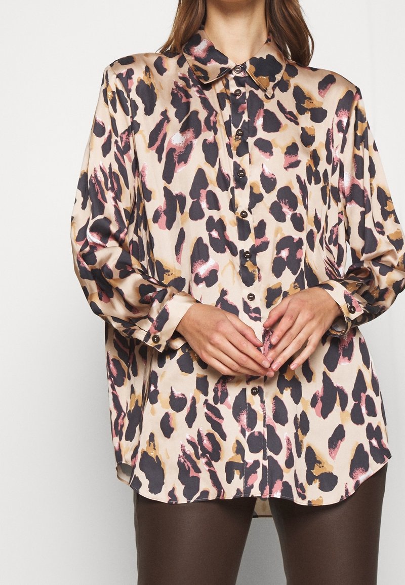 Blouse à imprimé léopard beige, avec des motifs marron, noir et rose, fermeture à boutons sur le devant et col classique. Texture douce et soyeuse.