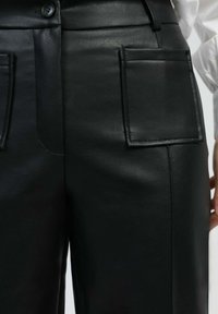 Pantalons en cuir noir présentant une texture lisse, des poches latérales, une fermeture à bouton à l'avant et des détails de coupe élégants.