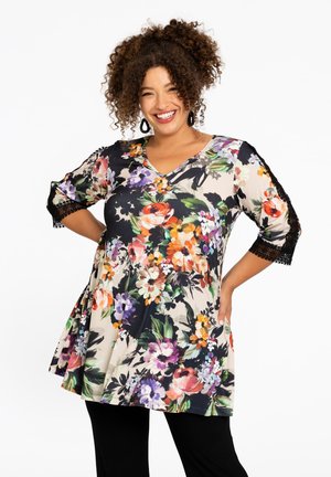 Tunique florale avec un décolleté en V, affichant un schéma de couleurs noir et crème, des motifs de fleurs colorés et des accents en dentelle sur des manches trois-quarts.