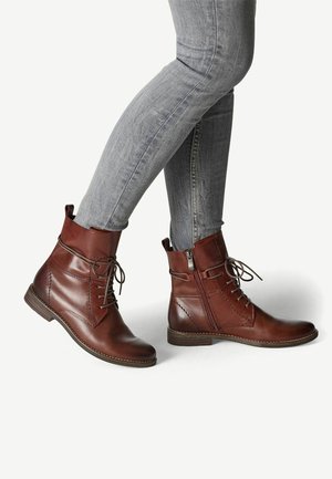 Bottes de cheville en cuir marron avec un bout rond, un laçage à l'avant, une fermeture éclair sur le côté et des détails de couture contrastants. Montées sur un talon bas.