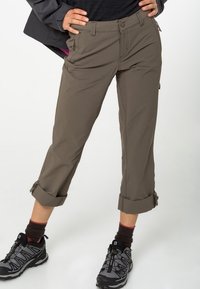 Pantalones de senderismo caqui, hechos de tejido ligero, con puños enrollados, trabillas para el cinturón y múltiples bolsillos para utilidad. Combinados con zapatos de senderismo.