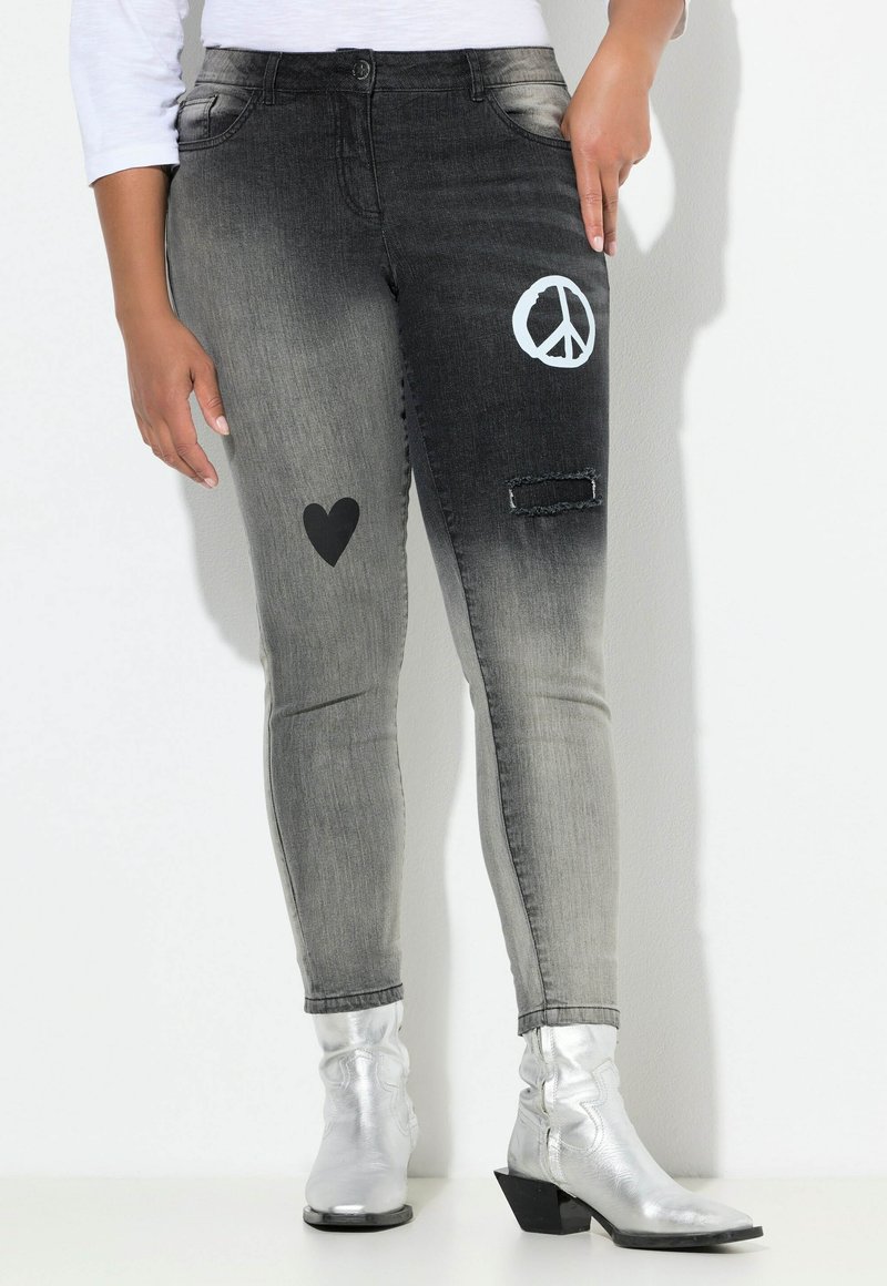Jeans de gradiente negro y gris con parches: un corazón, un símbolo de paz y una zona destrozada. Tienen una cintura de media altura y un corte ajustado.