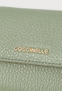 Green textured leather wallet with gold "Coccinelle" branding. Features a smooth clasp and a stitched edge for durability.