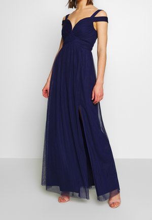 Robe maxi bleu marine avec bretelles tombantes, corsage froncé et longue jupe fluide avec une fente latérale. Tissu léger et texturé.