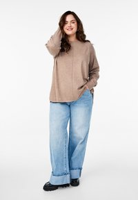 Bruine lange mouwen top met een ontspannen fit, gecombineerd met lichtblauwe wijde jeans en zwarte chunky laarzen. Eenvoudig ontwerp met een ronde halslijn.