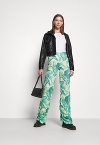 Jaqueta de couro preta cropped, blusa branca e calças flare com padrão em mármore verde. A modelo carrega uma pequena bolsa preta acolchoada e usa botas robustas.