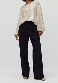 Haut à manches longues en sequins dorés associé à un pantalon large noir et des sandales à bout ouvert noires. Le tissu est brillant et texturé.