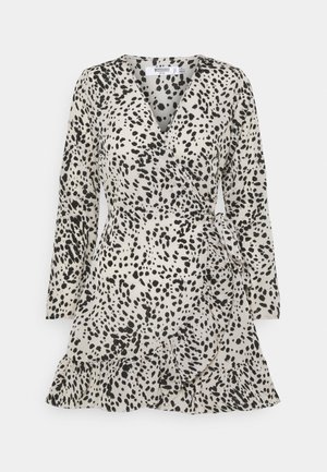 Robe longue à manches longues style portefeuille avec motif taches noir et blanc et ourlet à volants, nouée à la taille sur fond uni.
