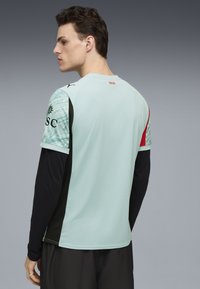 Urheilullinen lyhythihainen paita vaaleansinisellä värillä ja mustilla aksenteilla. Paidassa on kuvioidut hihat ja punaisia yksityiskohtia takana. 95 % polyesteria, 5 % elastaania.