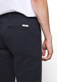 Donkerblauwe katoenen broeken met een achterzak waarop het label "forét" staat. De stof heeft een zachte textuur en een slim fit ontwerp.