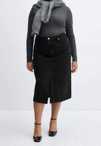 Falda midi de mezclilla negra con una abertura frontal, combinada con una blusa gris de manga larga y una bufanda gris, acompañada de tacones de charol negros.