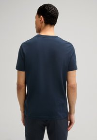 Granatowa bawełniana koszulka, krótki rękaw, okrągły dekolt, gładka faktura, z jednolitym tyłem i minimalnymi detalami.