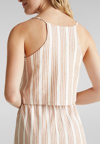 Valkoinen lyhennetty toppi, jossa pystysuuntaiset ruosteenväriset raidat, ohuet olkaimet ja suora selkäosa, esillä teksturoitu kangas.